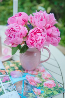 Açık bir kitabın üstündeki vazoda güzel pembe şakayıkların dikey görüntüsü.