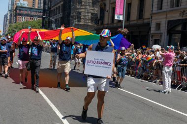 LGBT bayrakları ve geçit töreninde yürüyen gösteri tabelaları olan bir kalabalık.