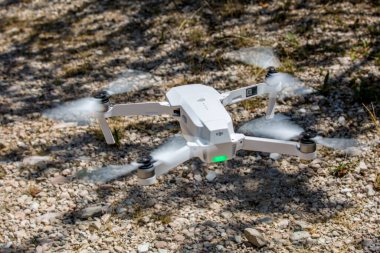 Aydınlık bir yaz gününde yerin üstünde uçan beyaz plastik bir dronun yakın çekimi.