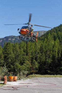 Chamonix Mont-Blanc Helikopteri yoğun ağaçlar ve kayalık dağlarla çevrili bir şekilde yerde uçuyor.