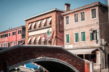Küçük bir köprü manzarası ve arka planda İtalyan bayraklı binalar.