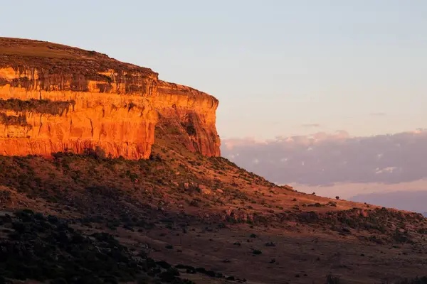 Kahverengi vadiye tepeden bakan bulutlu gün batımına karşı büyük dik kayalık bir uçurum.