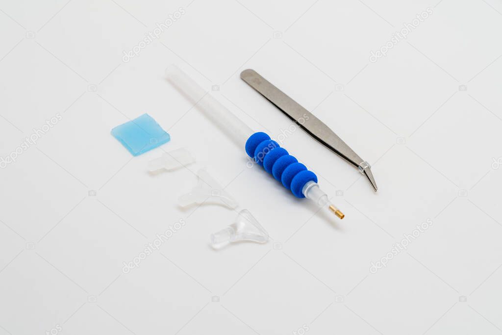Stainless steel tweezers and pen with several heads for diamond painting on a white background.