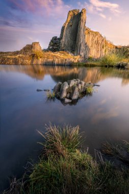 Gün batımında göl kenarında kayalık bir dağ.