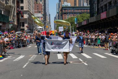 LGBT bayrakları ve geçit töreninde yürüyen gösteri tabelaları olan bir kalabalık.