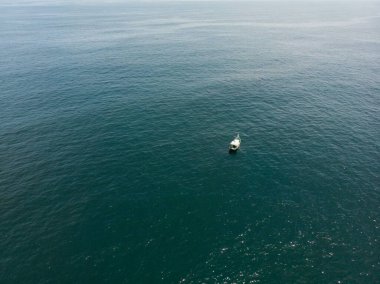 Güneşli bir günde mavi denizde yelken açan bir teknenin kuş bakışı görüntüsü.