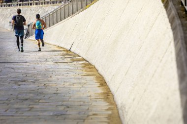Güneşli bir sabahta taş duvarın yanında koşan iki erkeğin arka çekimi.