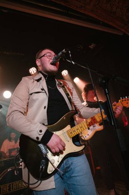 Lathums grubu konserde canlı performans sergiliyor, gitarist ve vokalist Alex Moore 'a odaklanıyor.