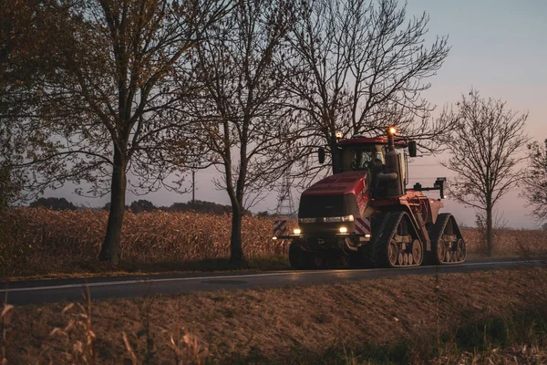 Červený Traktor Projíždějící Večer Kolem Prázdné Silnice — Stock fotografie