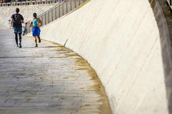 Güneşli bir sabahta taş duvarın yanında koşan iki erkeğin arka çekimi.