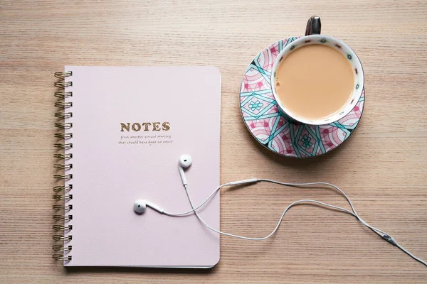 笔记本放在桌上 桌上放着白色耳机和一杯茶杯 还有粉红色的茶杯 还有办公用品 — 图库照片