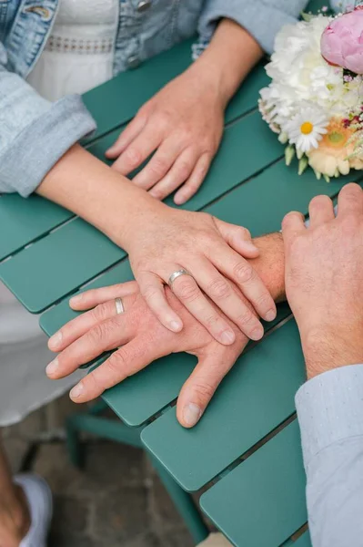 緑のテーブルの上に新郎の手に彼女の手を置く花嫁の垂直ショット — ストック写真