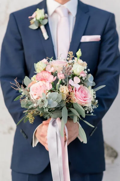 A closeup of groom with suit holding wedding bouquet with roses