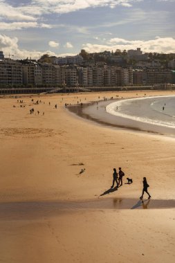 İspanya, San Sebastian 'ın kumlu plajında şehir siluetine karşı sahile gidenlerin dikey görüntüsü.