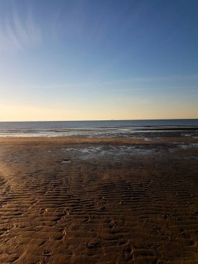 Su manzarası ve ufku olan kumlu bir sahilin dikey görüntüsü.