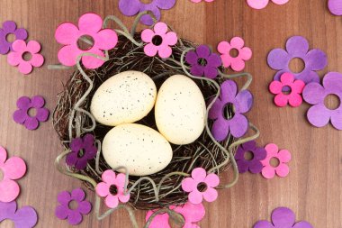 Ahşap bir masa üzerinde, leylak tonlarında yumurta ve çiçeklerle el yapımı Paskalya yuvası manzarası.
