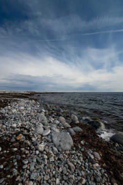 Jomfruland 'da bulutlu mavi gökyüzünün altındaki taşlı bir deniz manzarasının dikey çekimi.