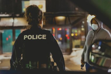 Bir kadın polis memuru, gece sokakta yerel bir kargaşa ihbarı için tanığa yaklaşıyor.