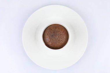 Beyaz arka planda klasik beyaz porselen bir ramekin içinde çikolatalı suflenin üst görüntüsü.