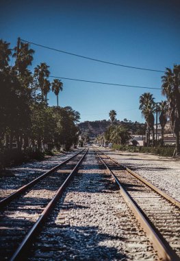 Demiryolları temiz gökyüzüne karşı binalar ve ağaçlarla çevrili.