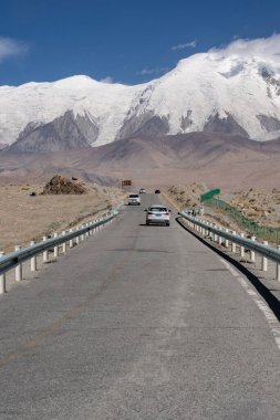 Arka planda dağlar olan asfalt yolda giden arabaların dikey görüntüsü.