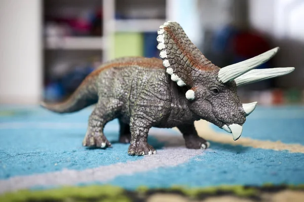 A closeup of a Triceratops Dinosaur toy on a blue rug