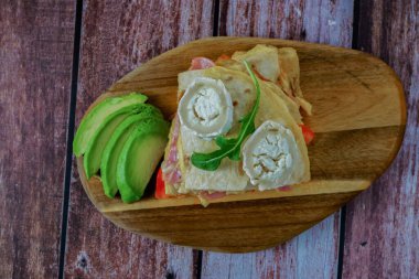 Domatesli sandviç, tortilla, jambon ve tahtanın üzerinde avokado ile keçi peyniri.