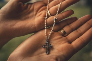 Altın yüzüklü insan palmiyesinde zincirli gümüş haçın sığ odak noktası.