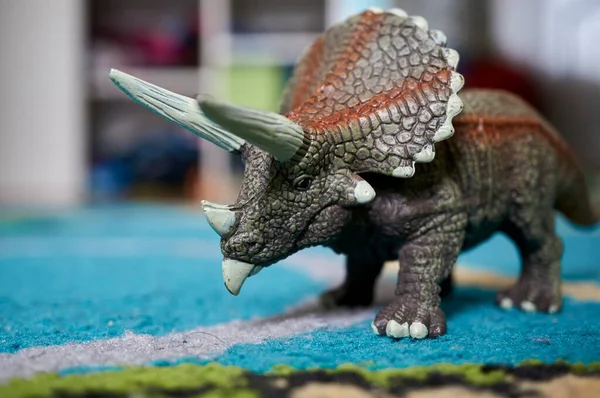 A closeup of a Triceratops Dinosaur toy on a blue rug