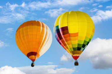 İki renkli sıcak hava balonu açık mavi gökyüzünde uçuyor.