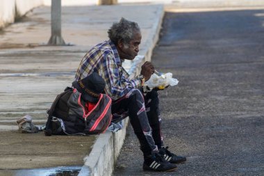Yaşlı bir adam kaldırımda oturuyor ve biraz sokak yemeği yiyor.
