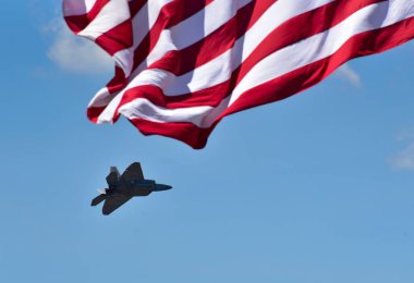 Mavi gökyüzü ve güneş ışığı altında Amerikan bayrağının alçak açılı görüntüsü ve askeri bir uçak.