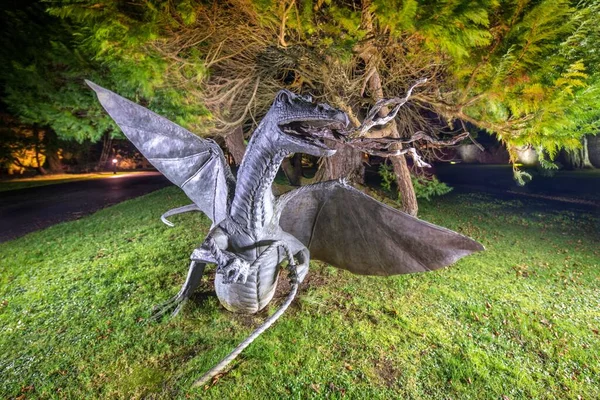 An old statue of a dragon with wings in a park at night