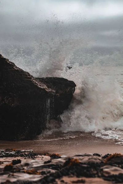 Pionowe Ujęcie Fal Morskich Uderzających Skały Plaży Pochmurną Pogodę — Zdjęcie stockowe