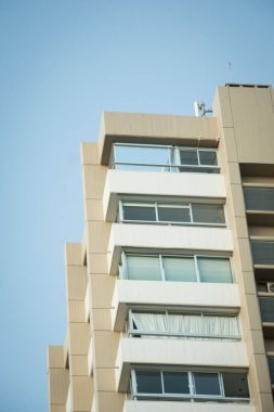 Mavi gökyüzüne karşı bej duvarları olan bir binanın dikey alçak açılı görüntüsü.