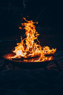 Geceleri kumlu bir sahilde metal bir kasede yanan şenlik ateşinin dikey görüntüsü.