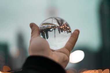 A closeup of a person's hand holding a glass ball with Downtown Toronto in the reflection clipart