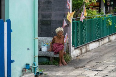 Bangkok sokaklarında oturan Taylandlı üstsüz bir adam. Yatay çekim