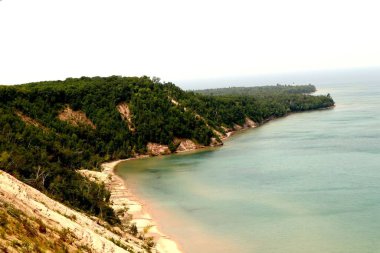 Gün batımında deniz suyunun yanında yeşil bir tepenin havadan görüntüsü.