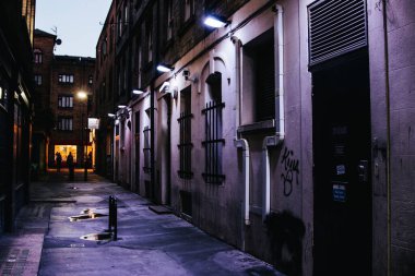 Beyaz sokak lambaları olan eski bir şehirde karanlık, dar bir cadde.
