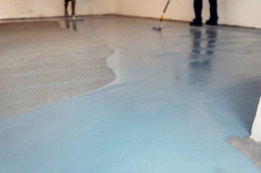 A construction worker apply grey epoxy resin in an industrial hall