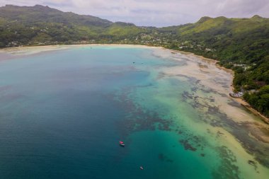 Seyşeller 'deki sakin su tesisinin etrafındaki mavi gökyüzünün altındaki yeşil tepelerin insansız hava aracı görüntüsü.