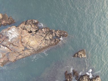 Küçük deniz dalgalarıyla kayalık bir sahilin insansız hava aracı görüntüsü.