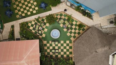 İnsanlar, sandalyeler, masalar, çıkıntılar ve ağaçlarla dolu bir avlunun havadan çekilmiş görüntüsü.