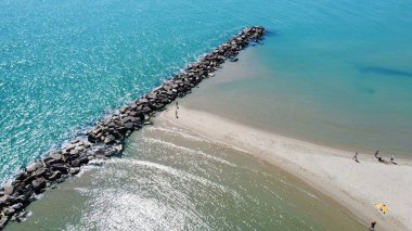 Dinlenen insanlarla dolu kumlu bir plajın ve berrak okyanusun hava aracı görüntüsü.