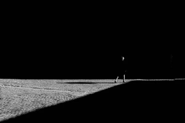 舗装スラブ上の影と街を歩く女性のシルエットのグレースケール — ストック写真