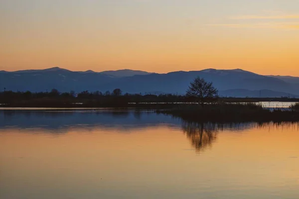 Uma Vista Panorâmica Lago Tranquilo Refletindo Árvores Nuas Montanhas Pôr — Fotografia de Stock