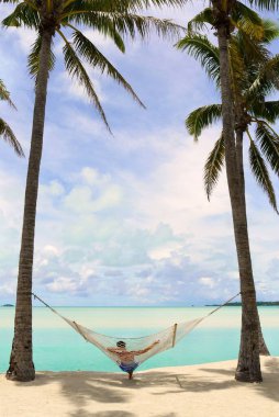 Hamakta uzanan bir insanın dikey görüntüsü palmiye ağaçlarına bağlanmış, güzel bir yaz gününde denizin tadını çıkarıyor.