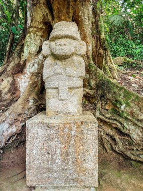 San Agustin Columbia 'da bir ağaç gövdesinin yakınındaki Moai heykelinin dikey görüntüsü.