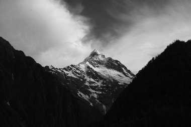 Bulutlu bir gökyüzünün altındaki dağların karlı zirvesi.